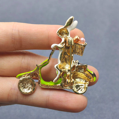 Back view of rabbit on a scooter brooch to show pin closure in a hand against a gray background
