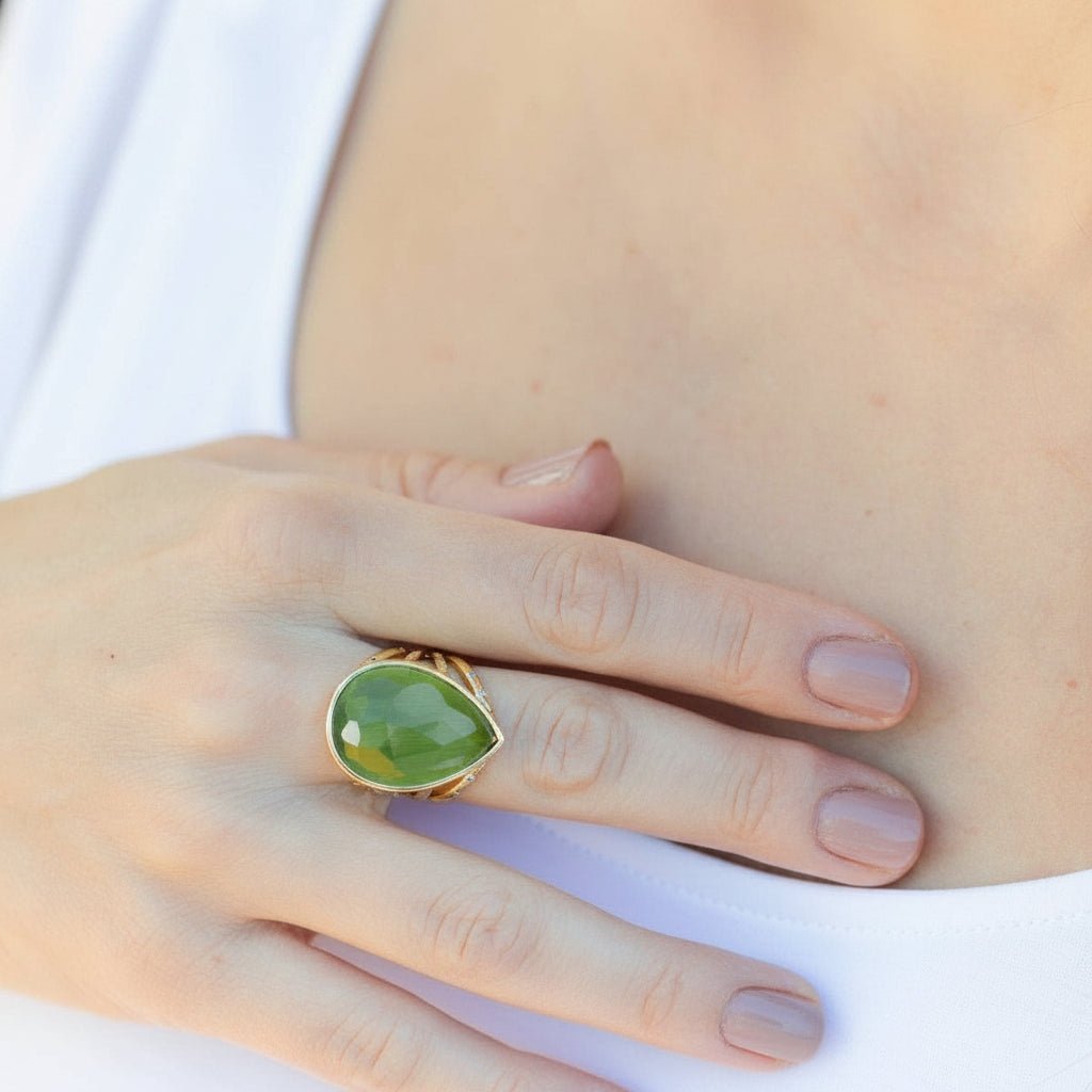 Hand wearing a green ring with gold band against a white tee shirt