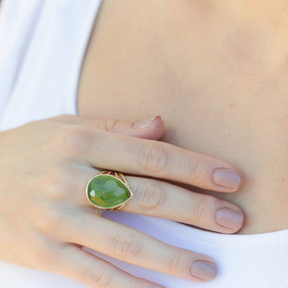 Hand wearing a green ring with gold band against a white tee shirt