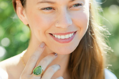 Woman wearing a green teardrop ring with a blurred green background