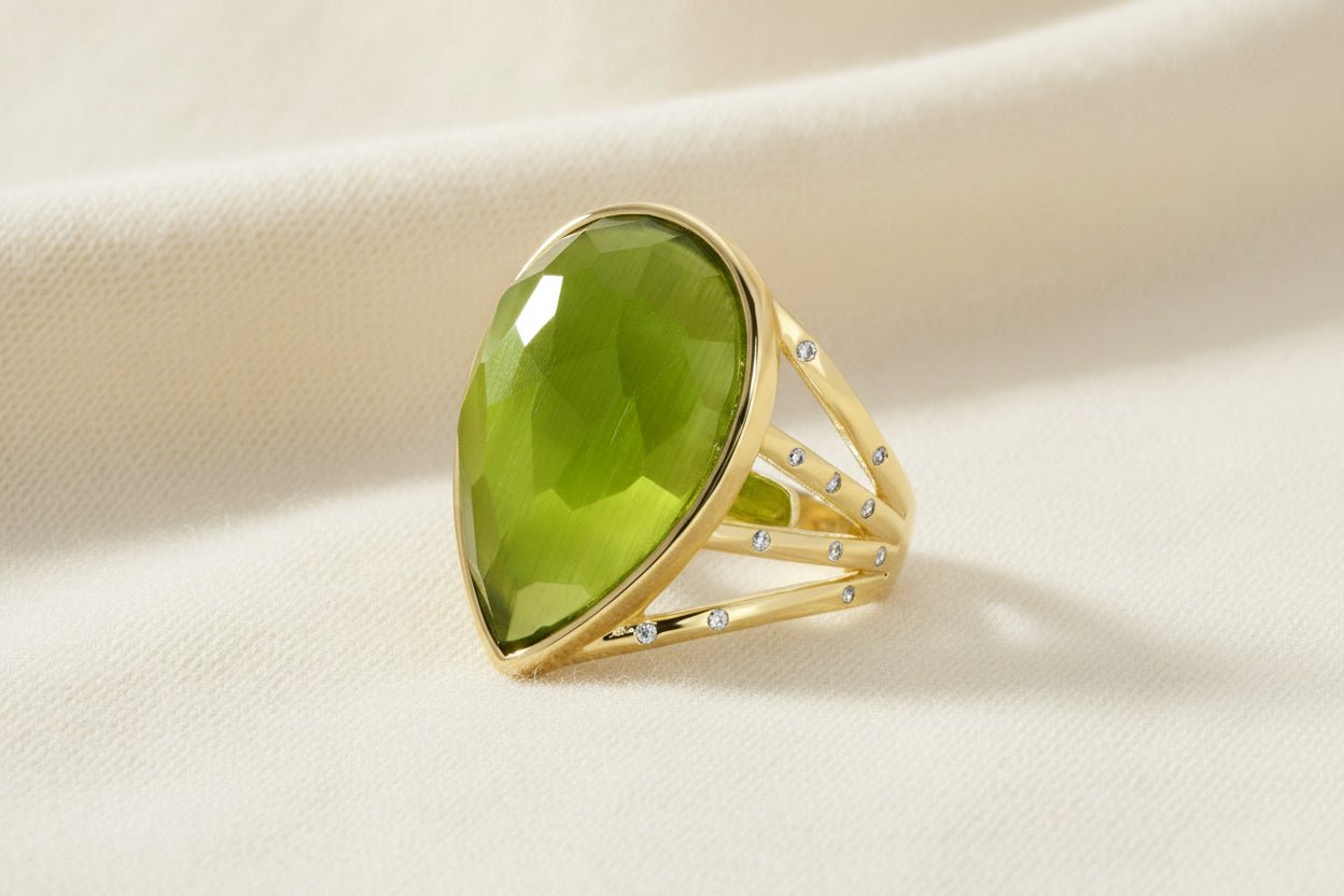 Gold ring with a large teardrop shaped green gemstone on a an ivory background