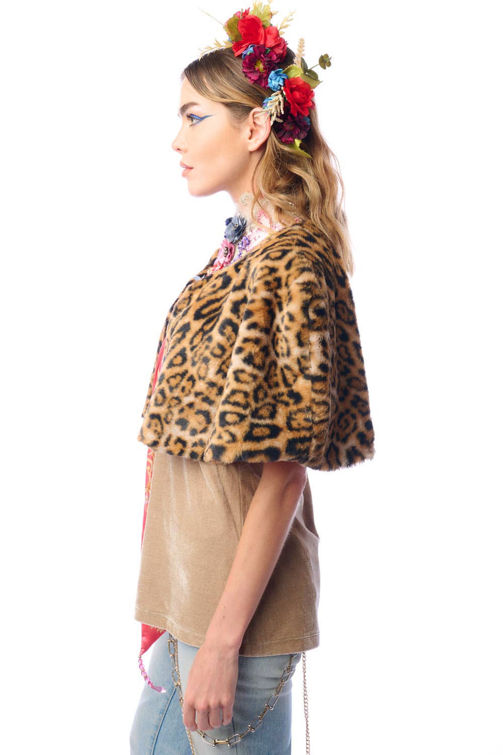 Side view of woman wearing a faux fur leopard print cape with a colorful flower headband on a white background