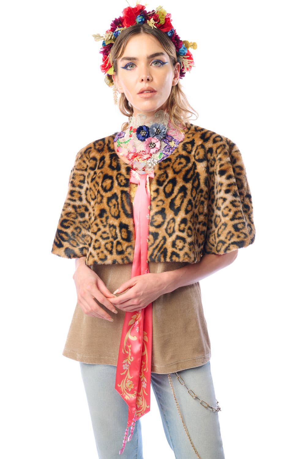 Woman wearing a faux fur leopard print cape with a colorful headpiece and floral scarf on a white background