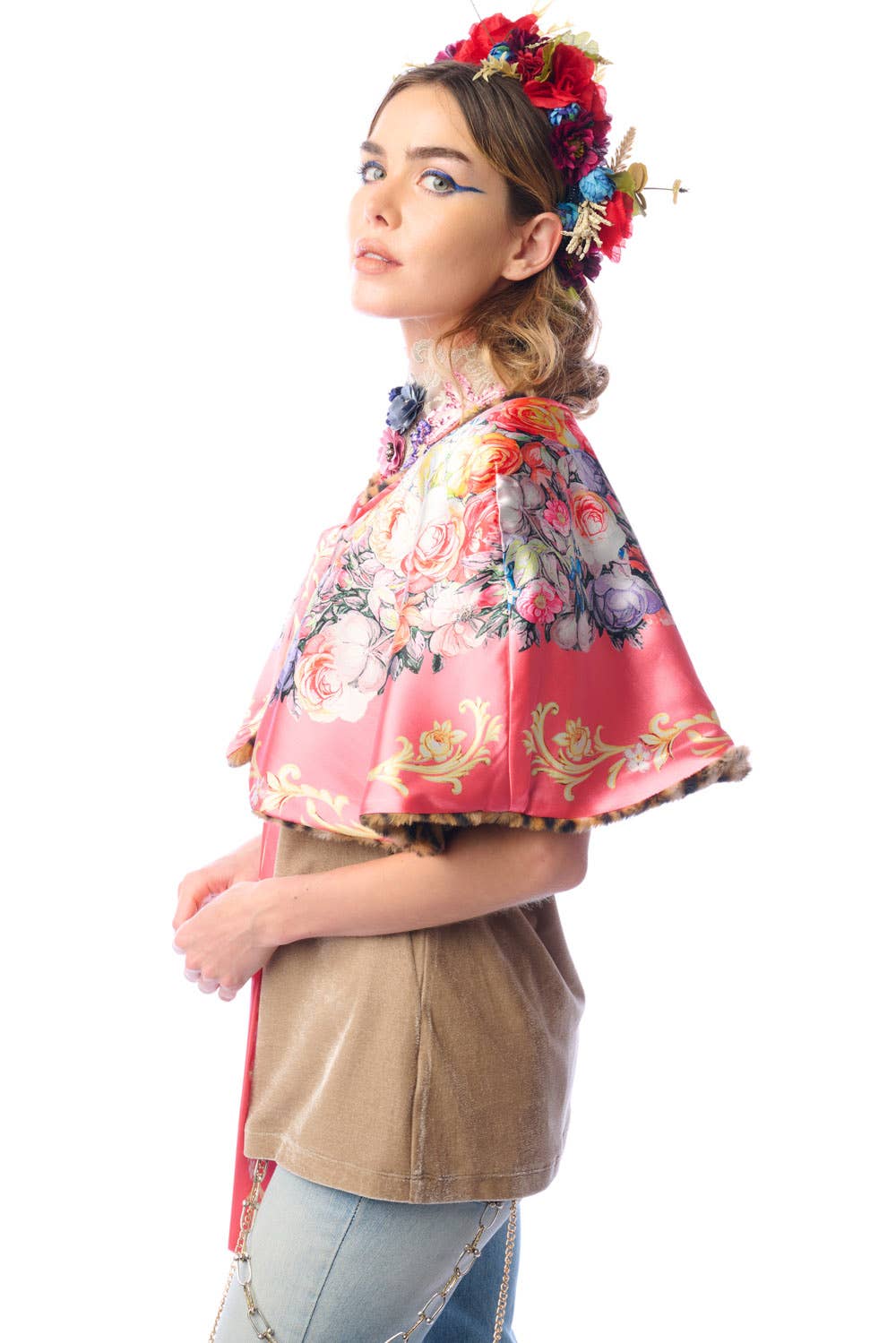 Side view of woman wearing a colorful reversible floral cape over a beige top on a white background