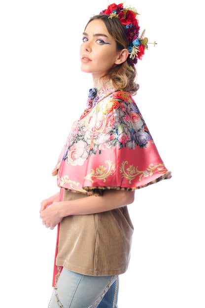 Side view of woman wearing a colorful reversible floral cape over a beige top on a white background