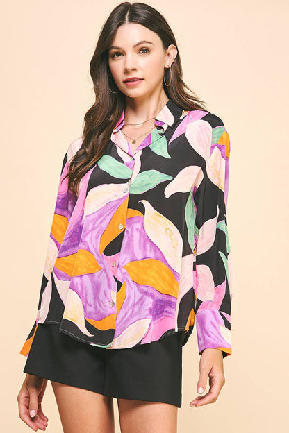 A woman wearing a multicolored floral button down blouse with long sleeves and black shorts.