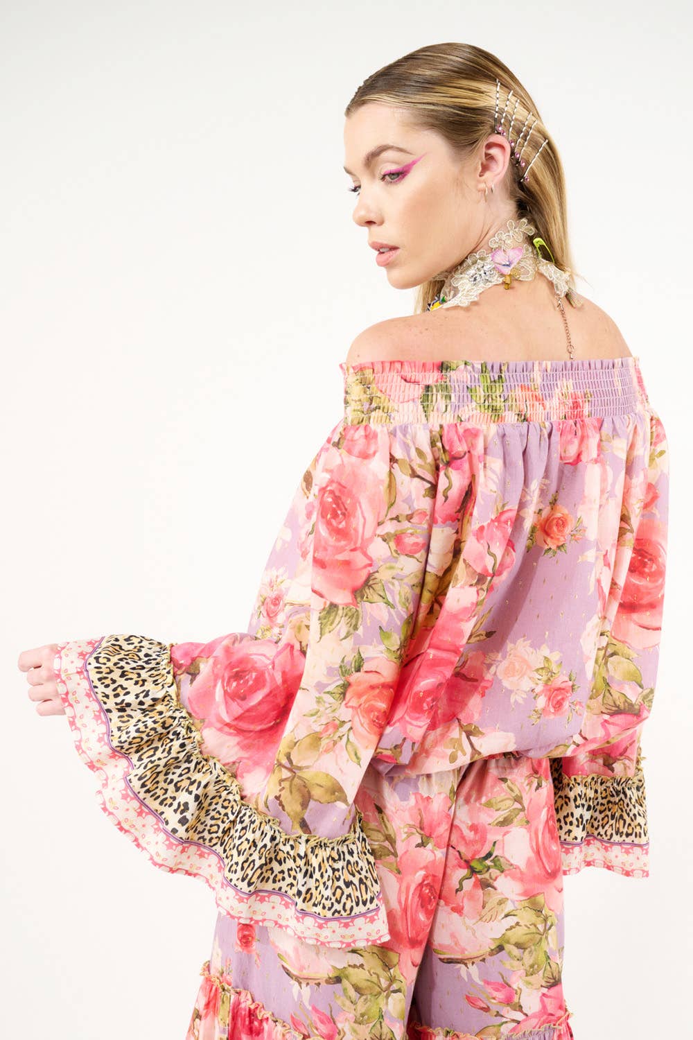 Woman wearing a floral off-shoulder top with leopard print details on a white background