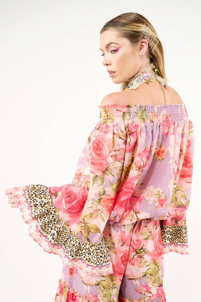Woman wearing a floral off-shoulder top with leopard print details on a white background