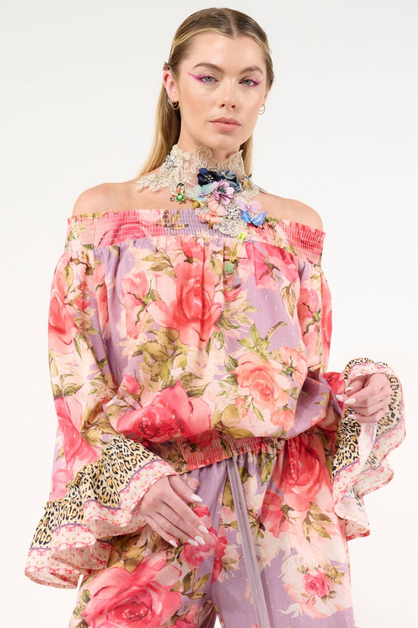 Woman wearing a floral off-shoulder top with intricate details on a white background