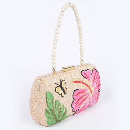 angled view of raffia bag with wood bead handle and floral and butterfly embroidery