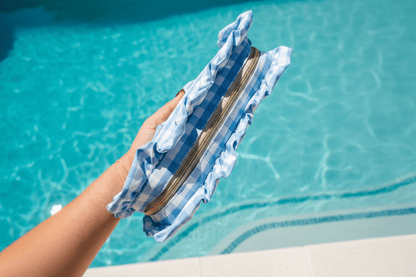 Blue and white checkered pouch with ruffles held by a hand with a pool in the background