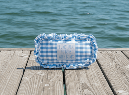 blue checkered cosmetic bag with a patch that reads "I only talk to boys with boats" sitting on a dock next to the ocean.