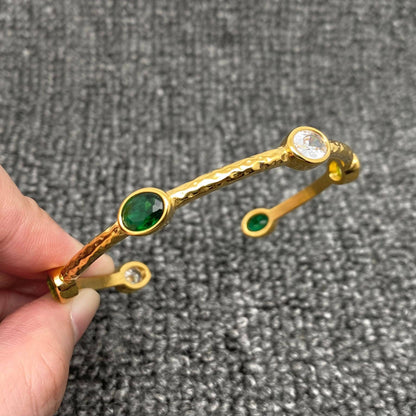 fingers holding a gold adjustable bangle with green and clear inlaid crystal stones