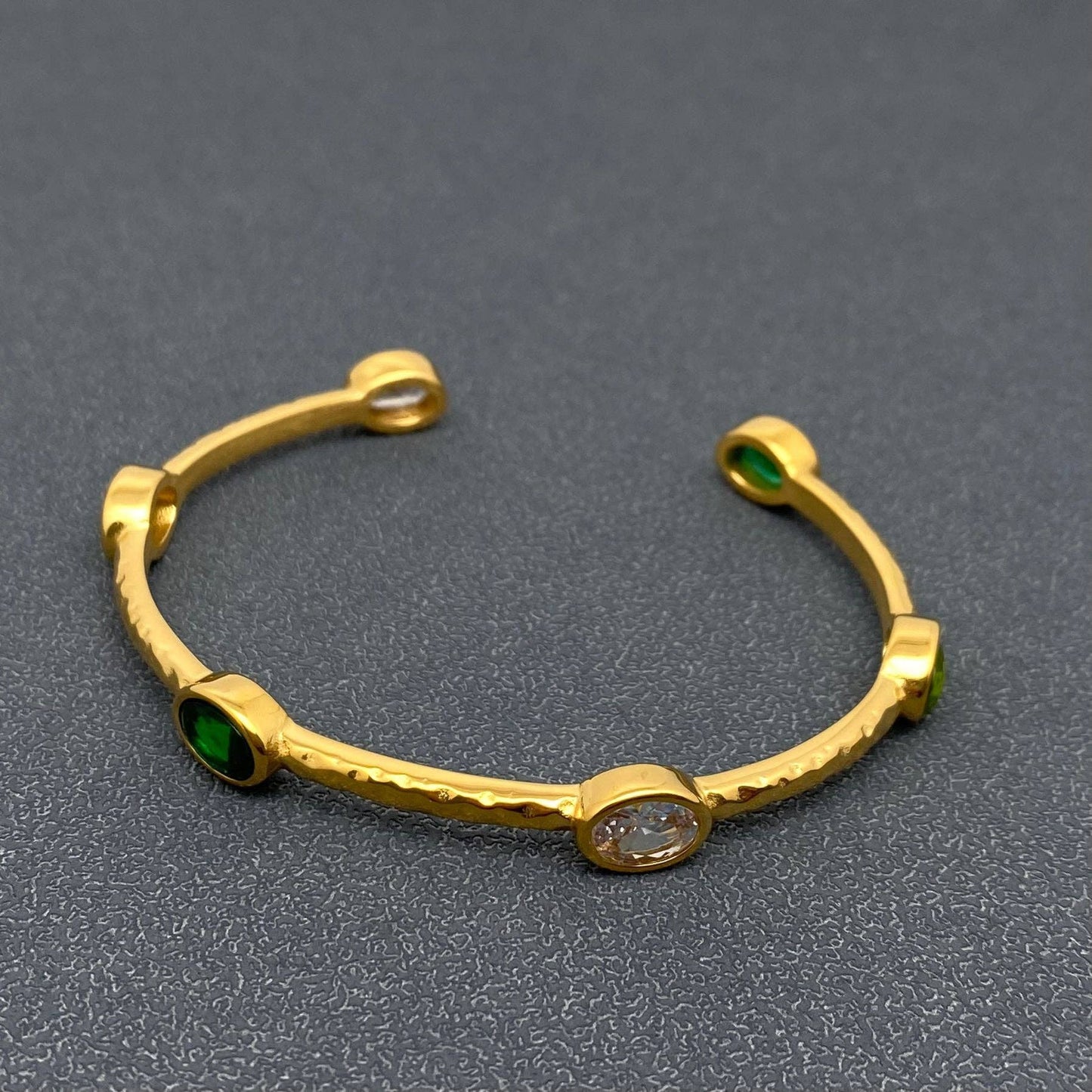 side view of a gold adjustable bangle with clear and emerald colored inlaid stones