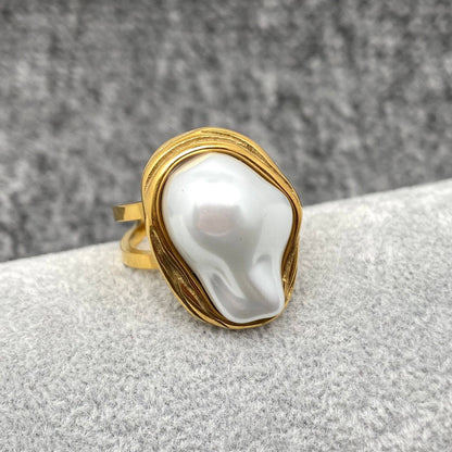 a gold adjustable ring with white baroque style pearl laying on a grey background