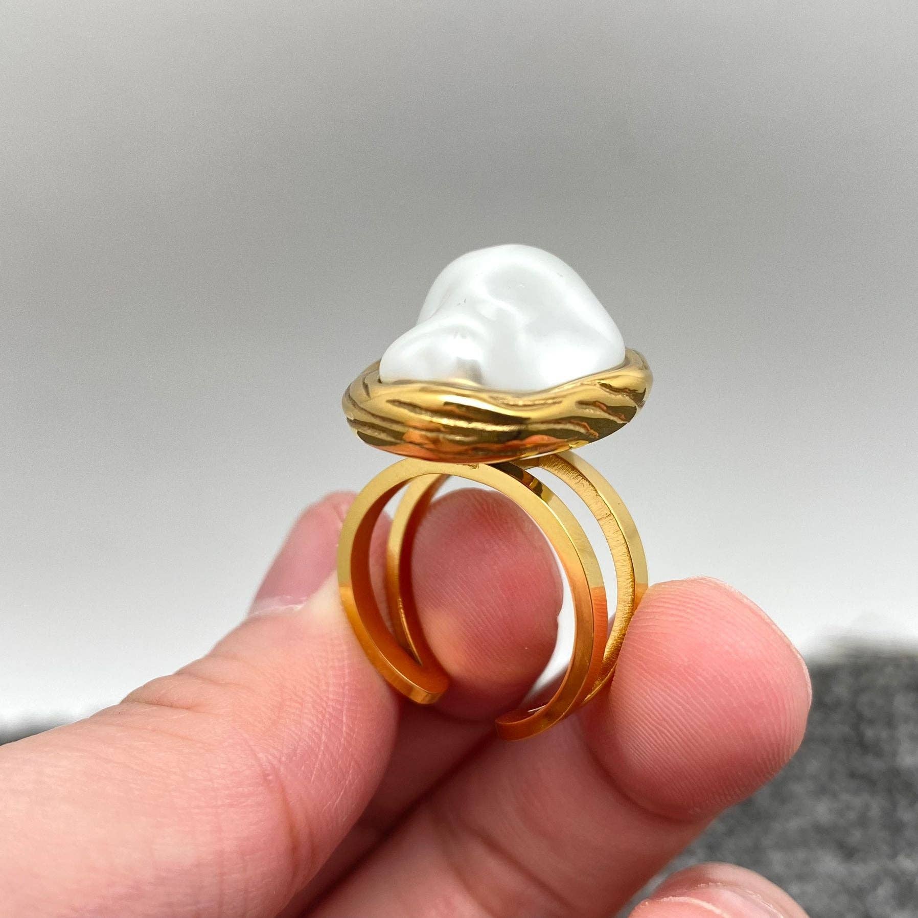 fingers holding a gold adjustable ring with white baroque style pearl to show the side profile of the ring