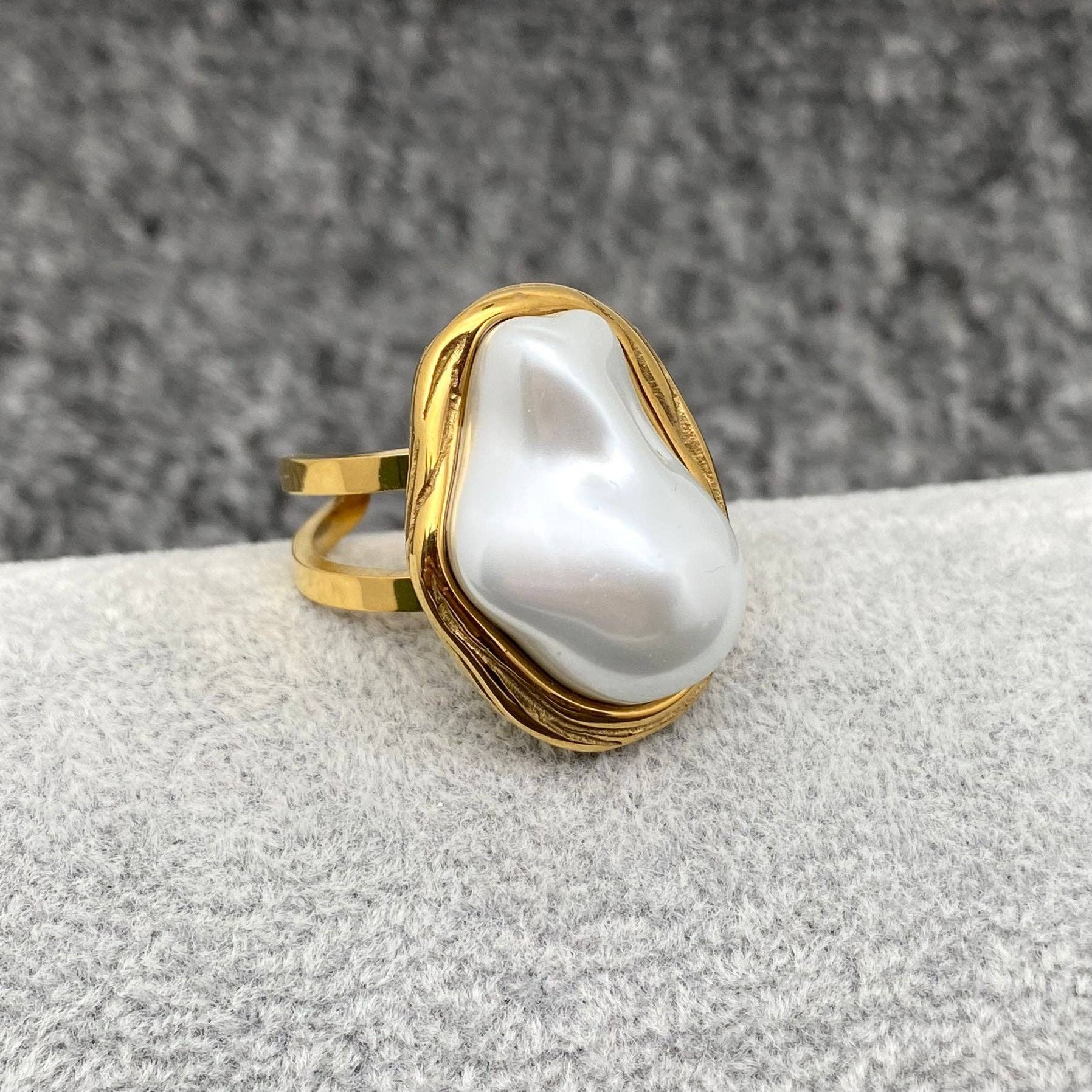 a gold adjustable ring with white baroque pearl laying on a grey background