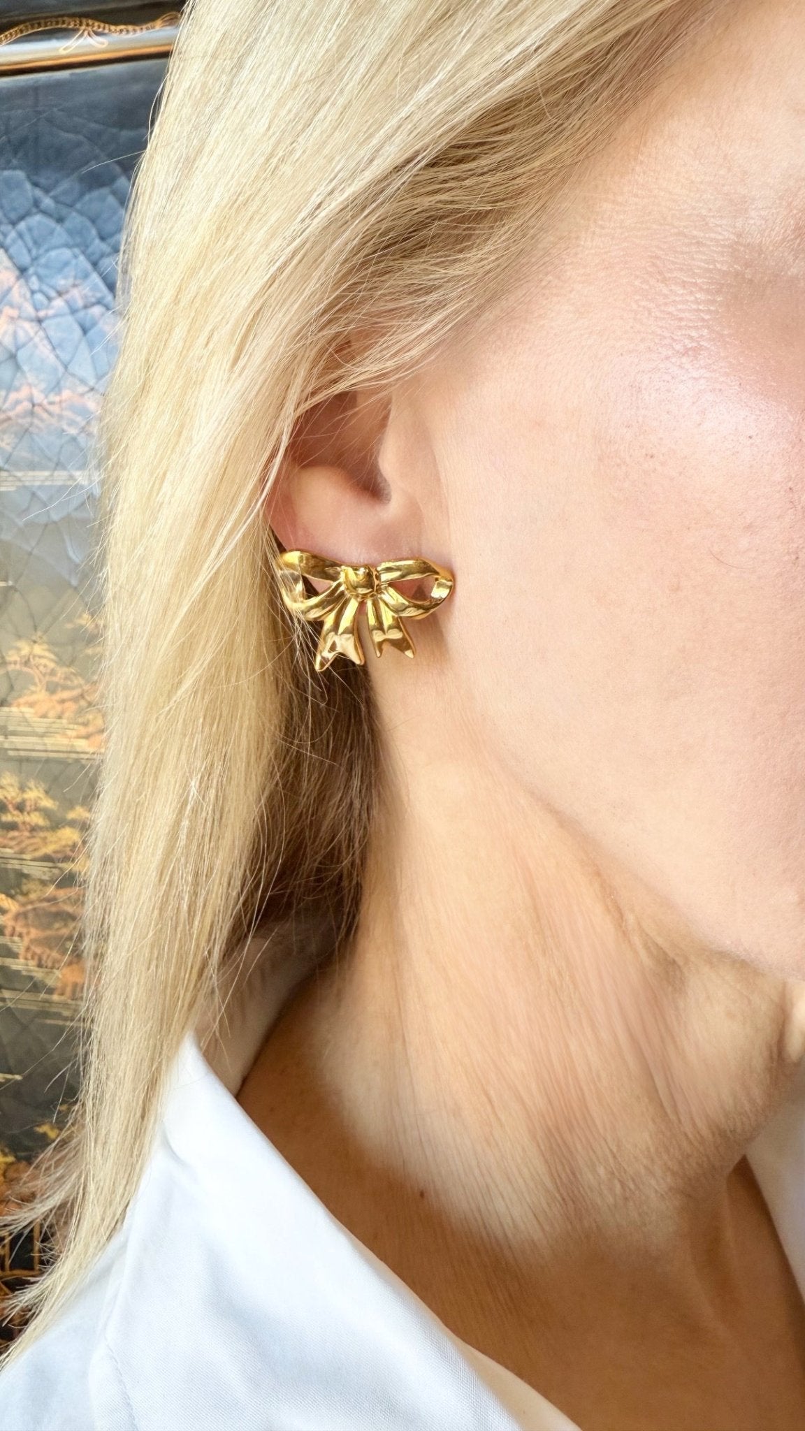 Gold bow-shaped earring worn by a person with blonde hair and a white shirt