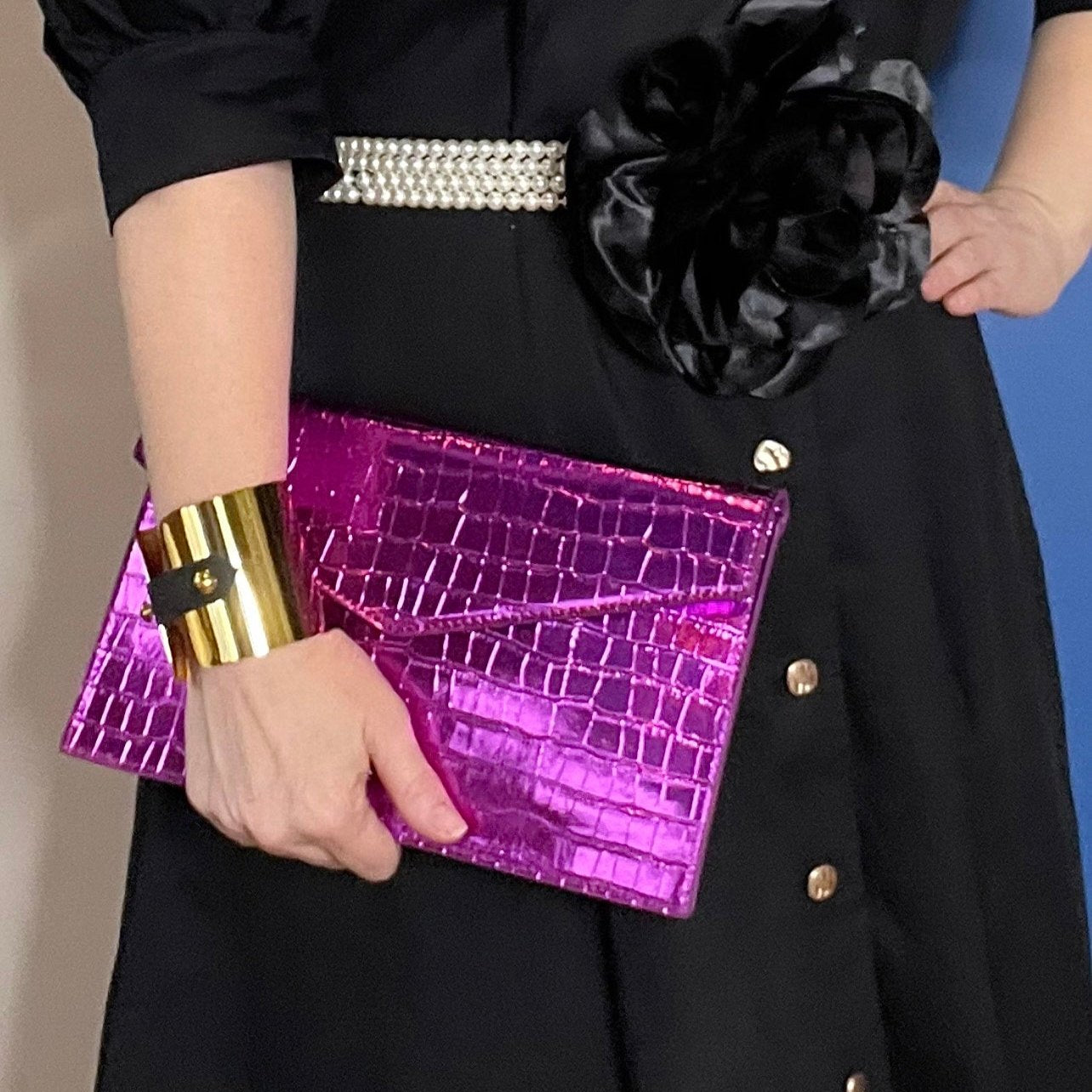 Woman wearing a black dress and magenta bag with brass cuff with black leather strap detail 
