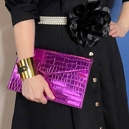Woman wearing a black dress and magenta bag with brass cuff with black leather strap detail 