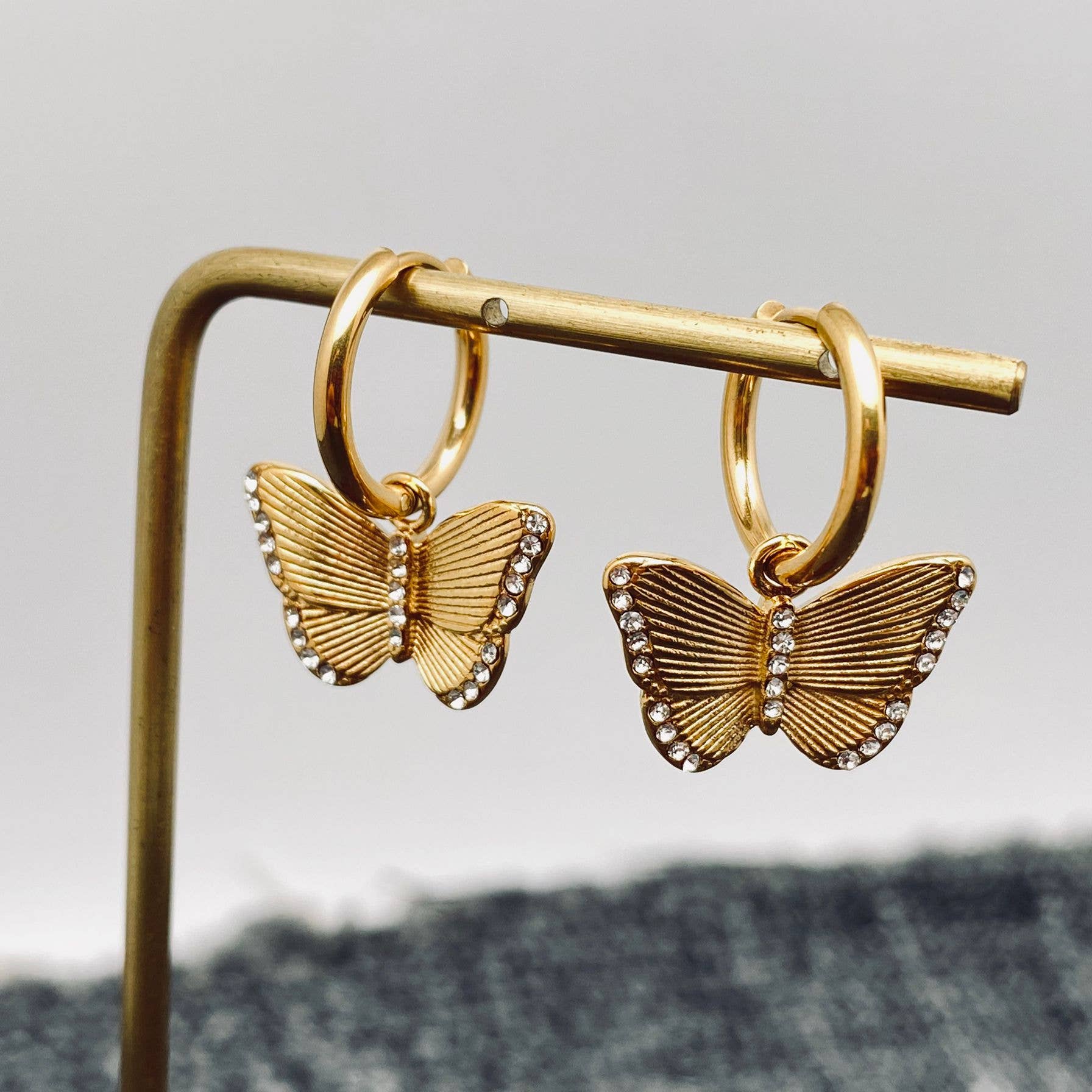 Gold butterfly crystal earrings on a stand with a neutral background