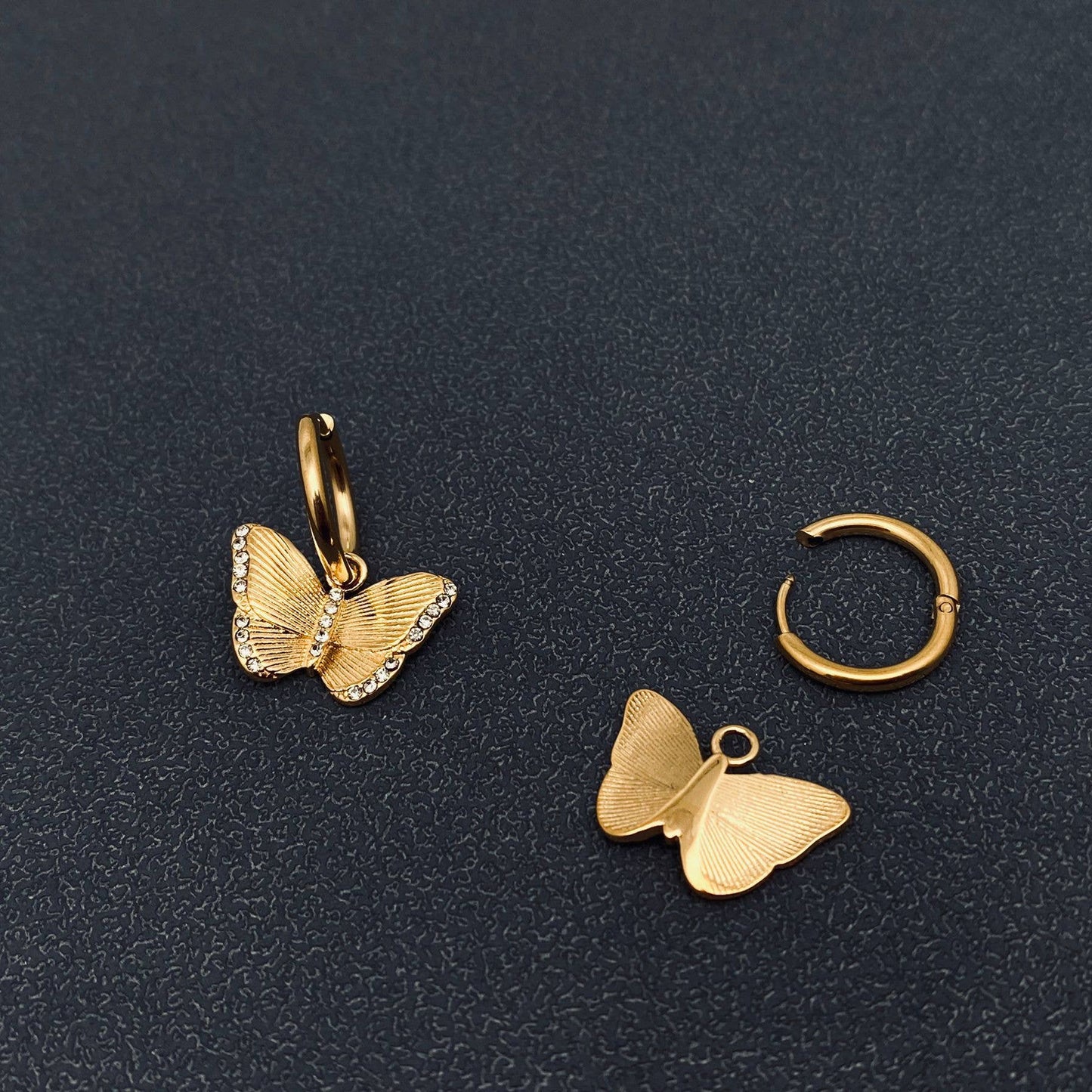 Front and back view of gold butterfly crystal earrings on a dark textured surface