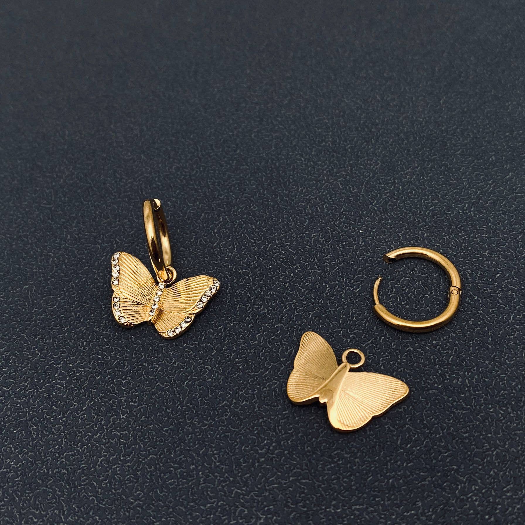 Front and back view of gold butterfly crystal earrings on a dark textured surface