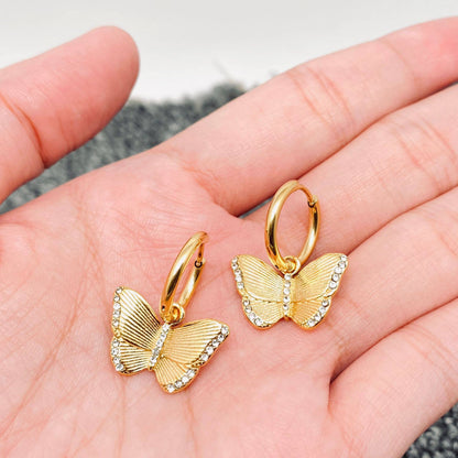 Gold butterfly and crystal dangle earrings held in a hand with a neutral background
