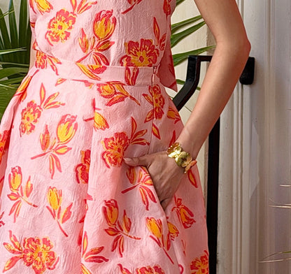 Person wearing a pink floral dress with a gold butterfly motif bracelet, standing outdoors