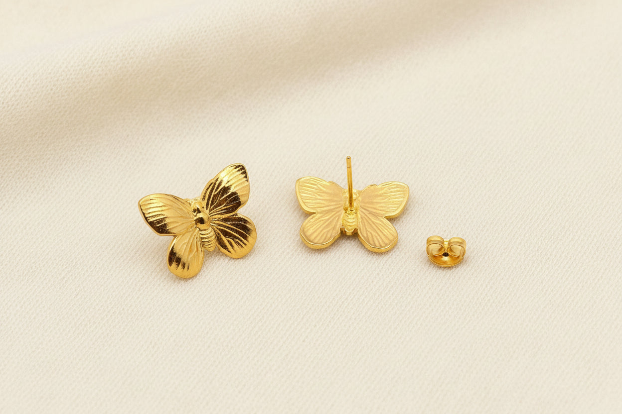 close up of front and back views of gold butterfly stud earrings on an ivory background