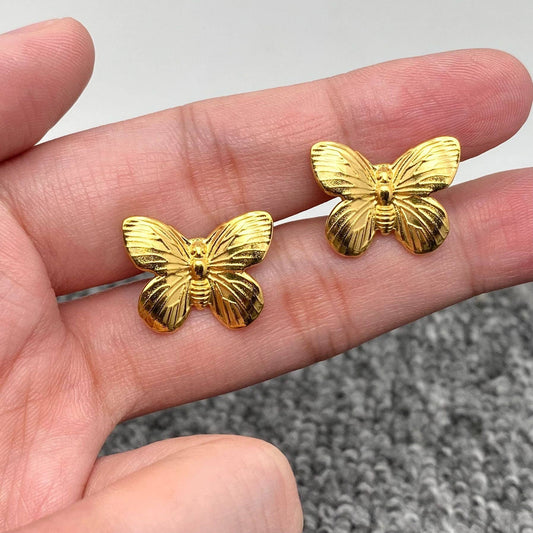 Gold butterfly stud earrings held in hand showing size and detail