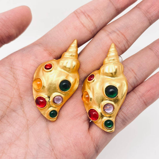 gold conch shaped earrings with inlaid multi glass stones on human hand