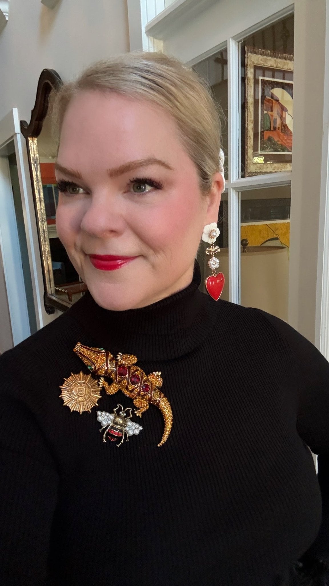 Person wearing a black turtleneck with 3 decorative brooches featuring a bee, sunburst, and alligator