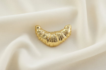 gold croissant shaped brooch on an ivory fabric background