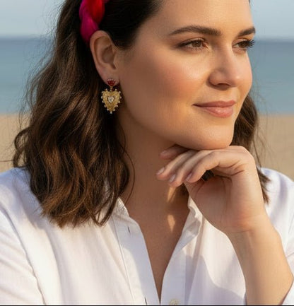 Woman wearing a red and pink headband and gold heart crystal earrings in an outdoor beach setting