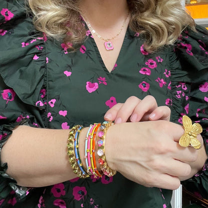 woman in floral blouse wearing gold cuff bracelets in various sizes and a gold butterfly ring