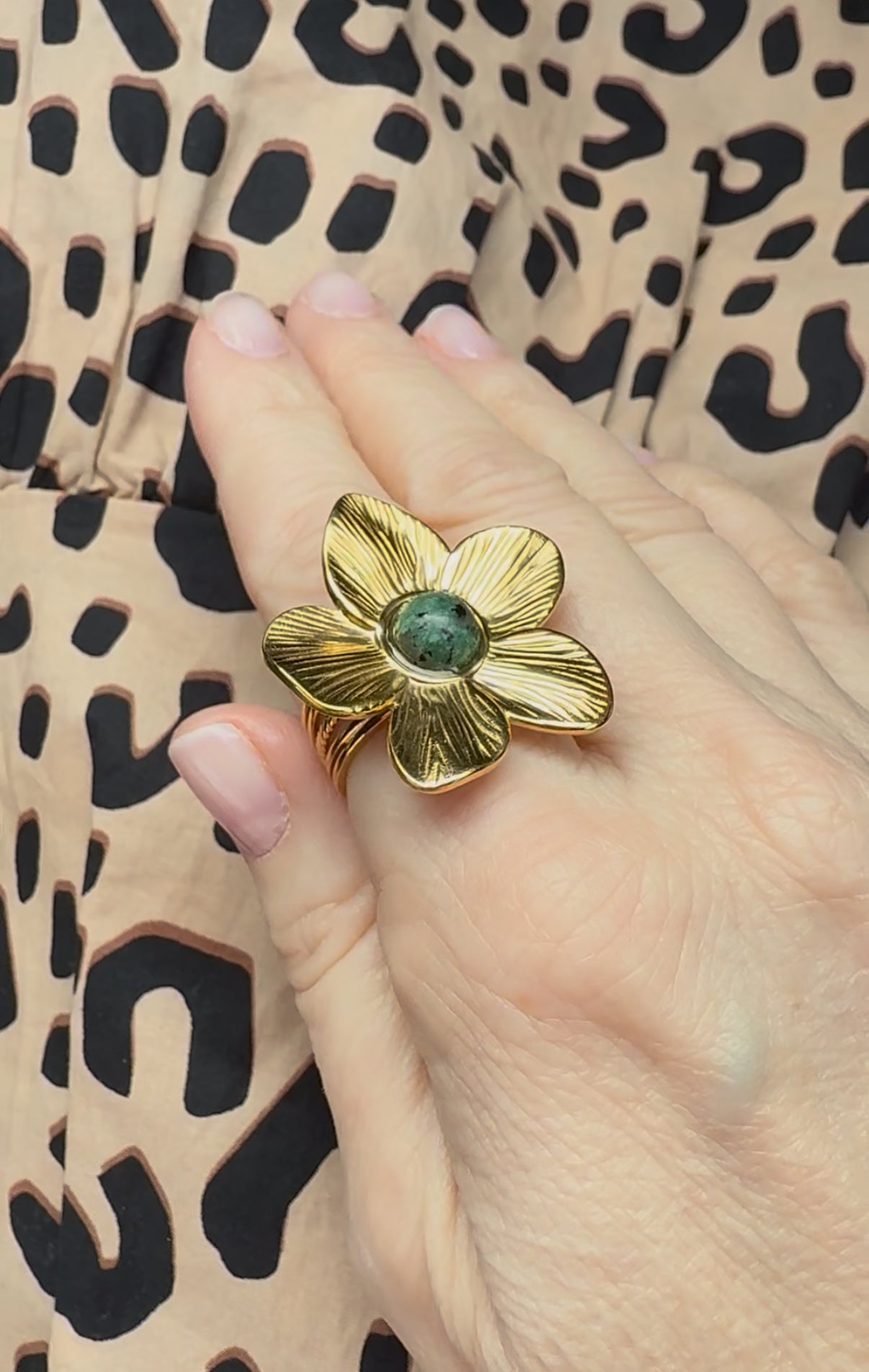Gold flower-shaped ring with a green african turquoise on a hand against a leopard print background