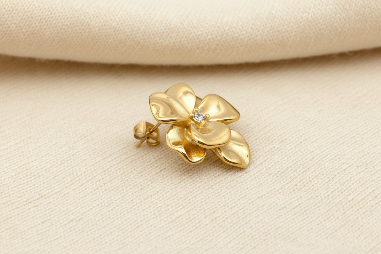 Gold flower-shaped earring on an ivory fabric background
