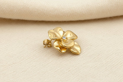 Gold flower-shaped earring on an ivory fabric background