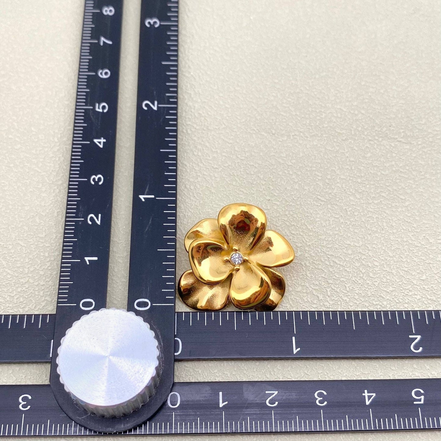 Gold flower-shaped jewelry piece with a diamond on a ruler for scale.