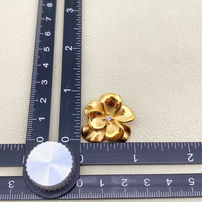 Gold flower-shaped jewelry piece with a diamond on a ruler for scale.