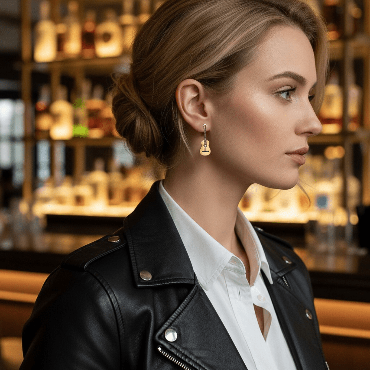 Woman wearing a black leather jacket and white shirt and gold guitar shaped earrings with a bar in the background