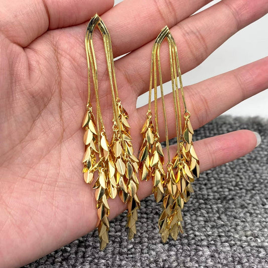 Gold leaf-shaped dangle earrings held in a hand on a textured surface