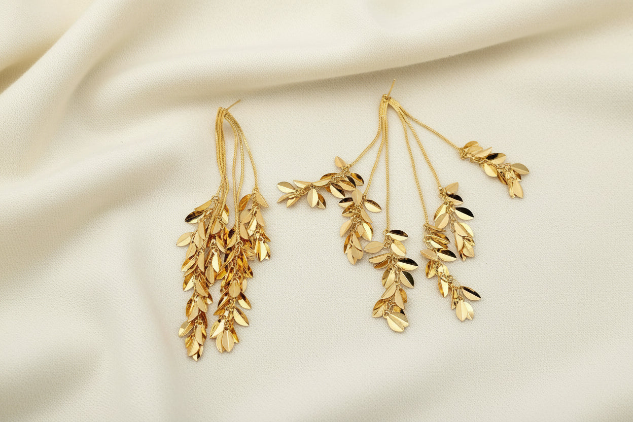 Pair of gold leaf dangle earrings on an ivory fabric background