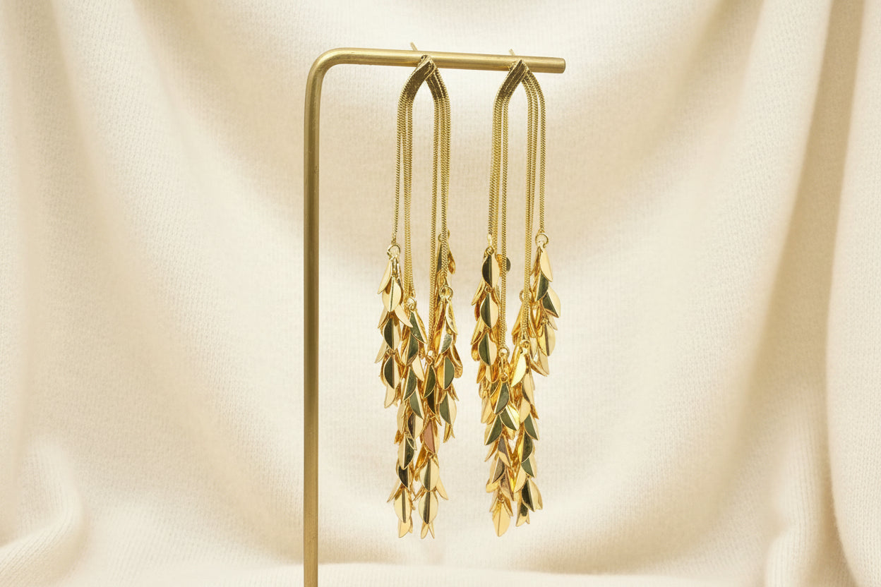 Gold leaf-shaped dangle earrings on a stand with a neutral background