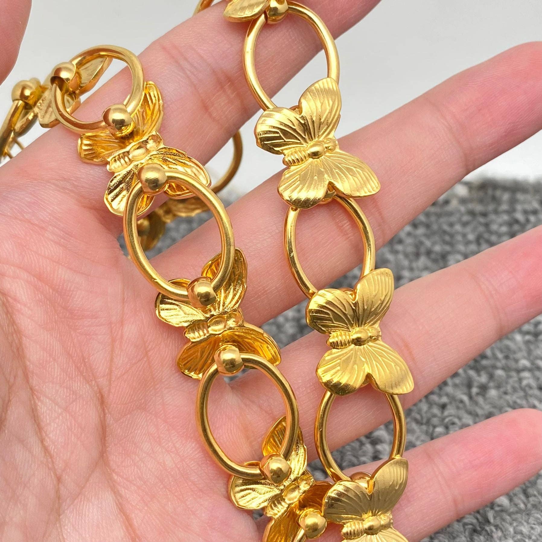 a hand holding a gold necklace with butterflies and circle links