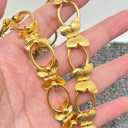 a hand holding a gold necklace with butterflies and circle links