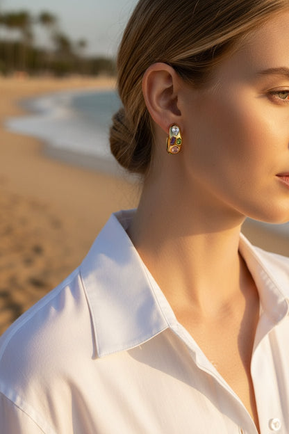 Gold hoop earrings with colorful gemstones on a woman in an outdoor beach setting