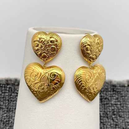 a pair of gold embossed double heart earrings hanging on a white vase