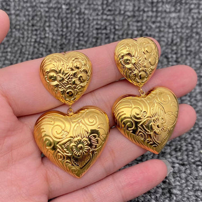 a pair of embossed gold heart earrings in the palm of a hand